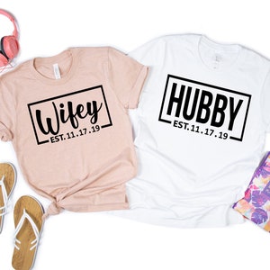 May include: Two t-shirts, one pink and one white, with the text "Wifey - EST. 11.17.19" and "Hubby - EST. 11.17.19" printed on them.