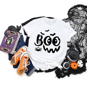 Puede incluir: Camiseta blanca con un gr&aacute;fico negro de un fantasma sonriente con la palabra "BOO" y una ara&ntilde;a con una telara&ntilde;a.