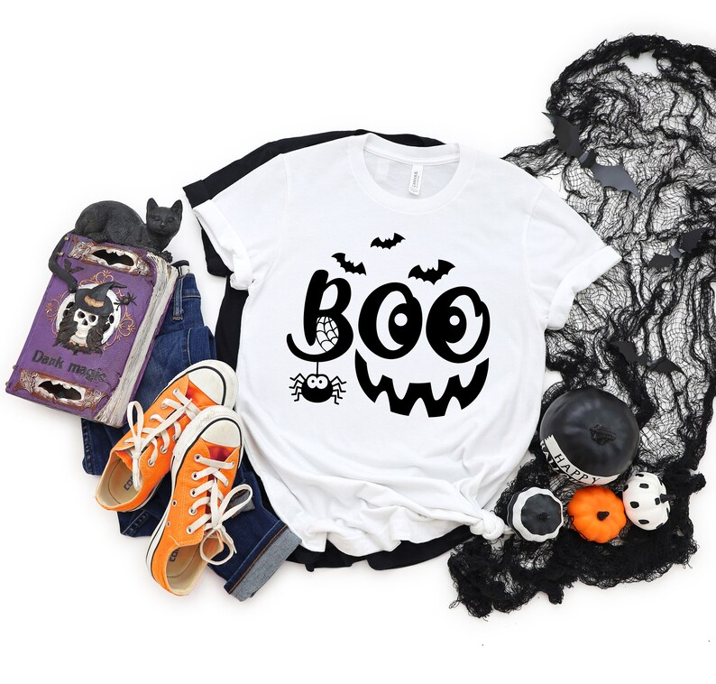 Puede incluir: Camiseta blanca con un gr&aacute;fico negro de un fantasma sonriente con la palabra "BOO" y una ara&ntilde;a con una telara&ntilde;a.