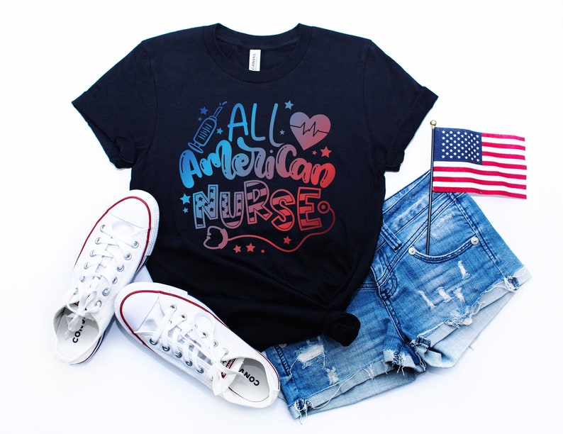 K&ouml;nnte beinhalten: Ein schwarzes T-Shirt mit dem Text "All American Nurse" in rot-wei&szlig;-blauem Farbverlauf. Das Shirt wird mit Jeans-Shorts, wei&szlig;en Sneakern und einer kleinen amerikanischen Flagge kombiniert.