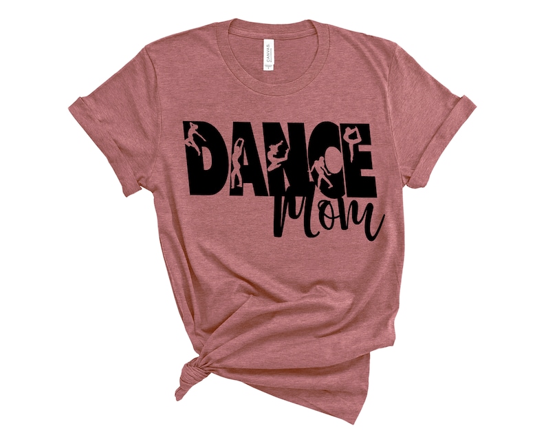 May include: A heather pink t-shirt with the text "Dance Mom" in black. The text is surrounded by silhouettes of dancers.