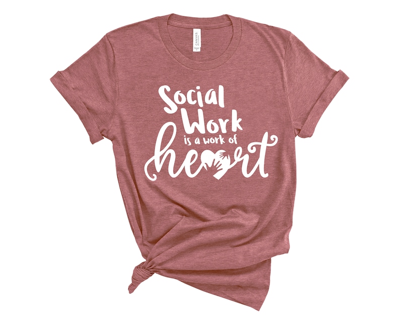 May include: A maroon t-shirt with the text "Social Work is a work of heart" in white lettering. The heart graphic features two hands holding each other.