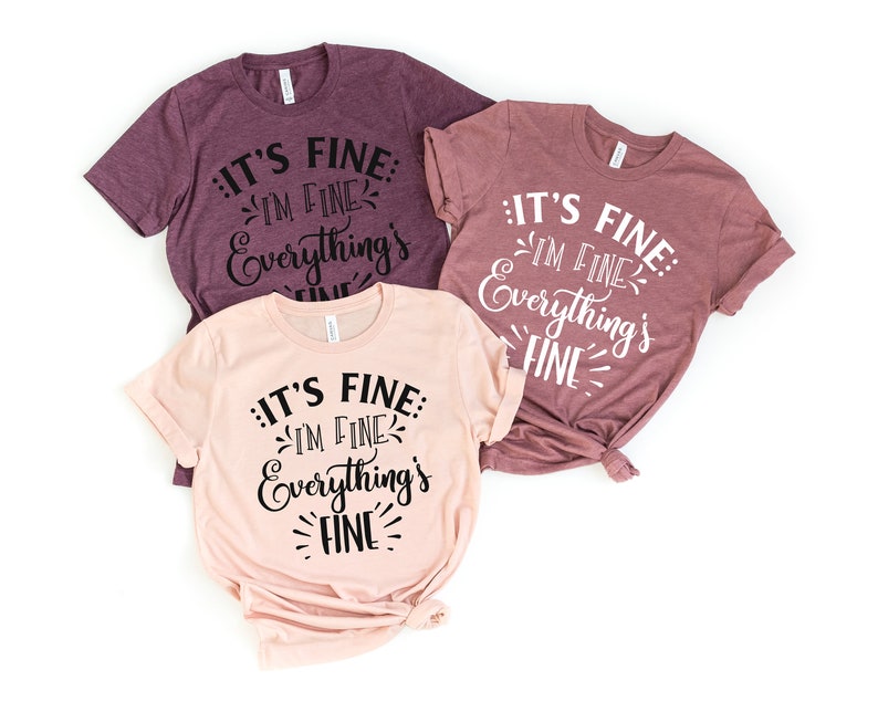 Peut inclure: Trois t-shirts avec le texte "It's fine: I'm fine. Everything's fine." en &eacute;criture cursive noire sur un fond rose et mauve.