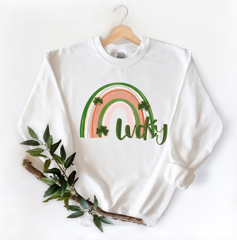 May include: White sweatshirt featuring a rainbow design with the word "lucky" in green lettering. The rainbow is decorated with green shamrocks.