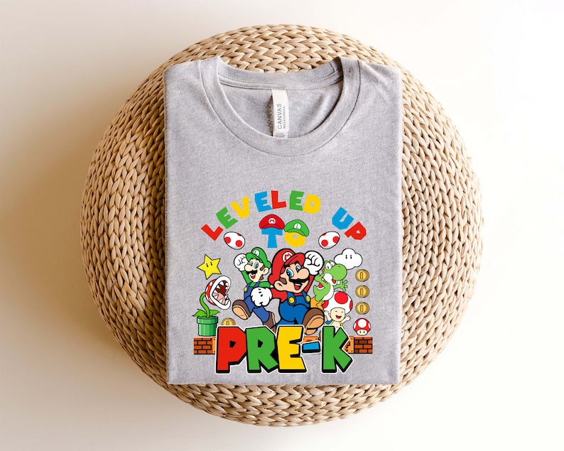 以下が含まれることがあります： スーパーマリオブラザーズのビデオゲームのキャラクター、マリオとルイージのグラフィックが描かれたグレーのTシャツ。グラフィックには「Leveled Up To Pre-K」と書いてあります。