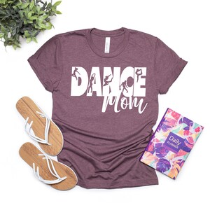 May include: A maroon t-shirt with the text "DANCE MOM" in white with a silhouette of dancers in the letters.