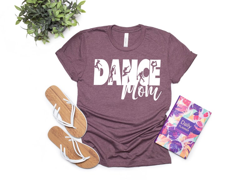 May include: A maroon t-shirt with the text "DANCE MOM" in white with a silhouette of dancers in the letters.