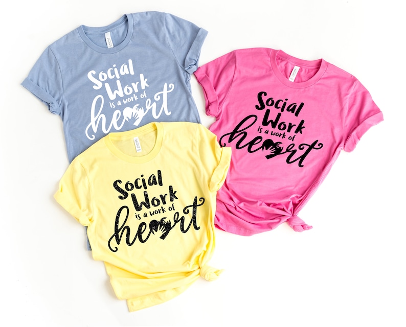 May include: Three t-shirts with the text "Social Work is a work of heart" in black lettering with a handprint heart graphic. The shirts are in blue, yellow, and pink.