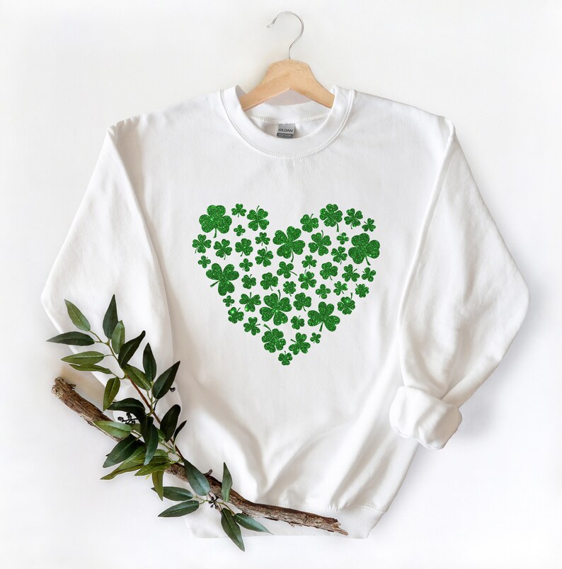 May include: White sweatshirt with a green glitter shamrock heart design. The shamrocks are arranged in a heart shape.