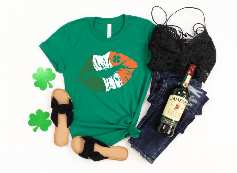 May include: Green t-shirt with a kiss graphic in the colors of the Irish flag, paired with black sandals, a black lace top, and dark wash jeans. A bottle of Jameson Irish Whiskey is also included in the image.