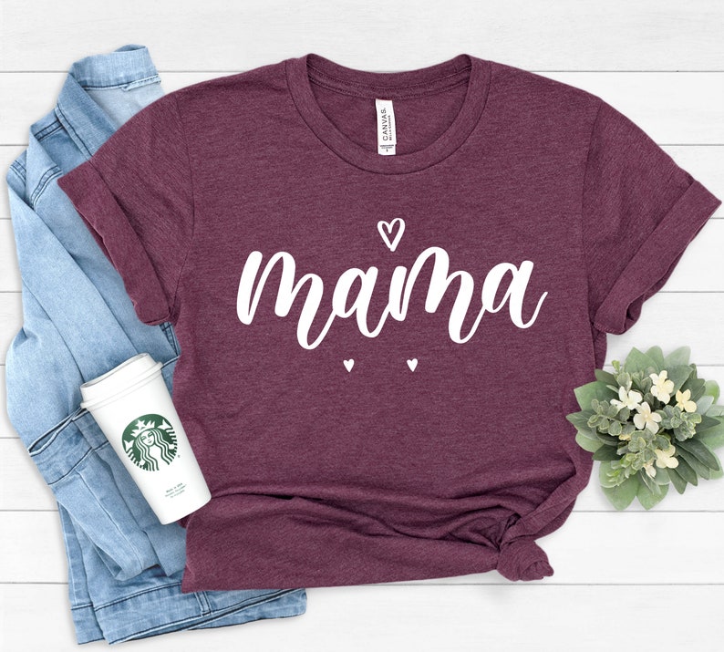 May include: A maroon t-shirt with the word "mama" written in white cursive lettering. There are small white hearts above and below the word.