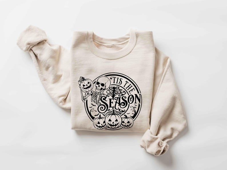 May include: A beige sweatshirt with a black graphic print of a skeleton holding a pumpkin and the text "Tis the Season".