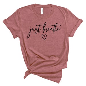 Puede incluir: Una camiseta de color malva con el texto "just breathe" en escritura negra con un peque&ntilde;o coraz&oacute;n debajo del texto.
