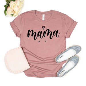May include: A mauve colored t-shirt with the word "mama" written in black cursive lettering. There are three small black hearts above and below the word.