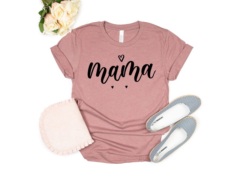 May include: A mauve colored t-shirt with the word "mama" written in black cursive lettering. There are three small black hearts above and below the word.