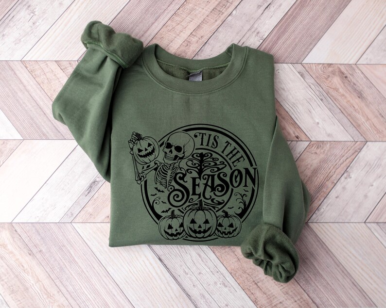May include: A green sweatshirt with a black graphic print of a skeleton holding a pumpkin and the text "Tis the Season".