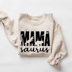 May include: A beige sweatshirt with a black graphic print that says "MAMA saurus" with dinosaur silhouettes.