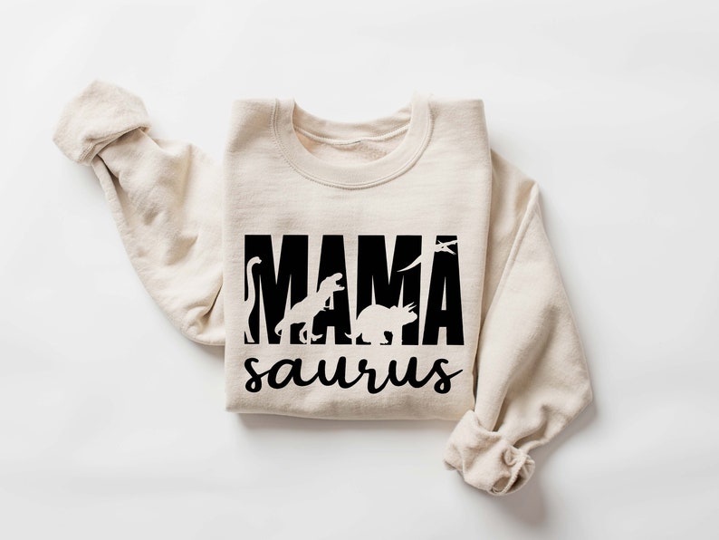 May include: A beige sweatshirt with a black graphic print that says "MAMA saurus" with dinosaur silhouettes.