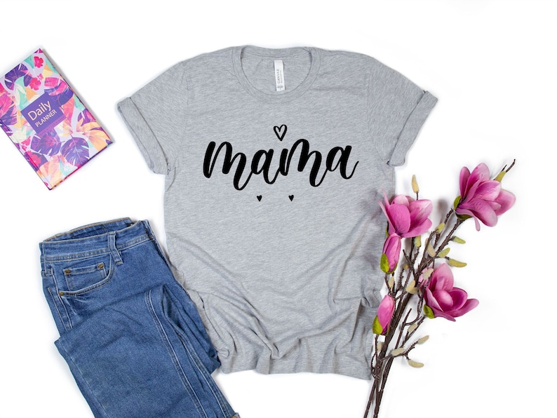 May include: Gray t-shirt with the word "mama" in black script with a small heart above the word and two smaller hearts below the word.