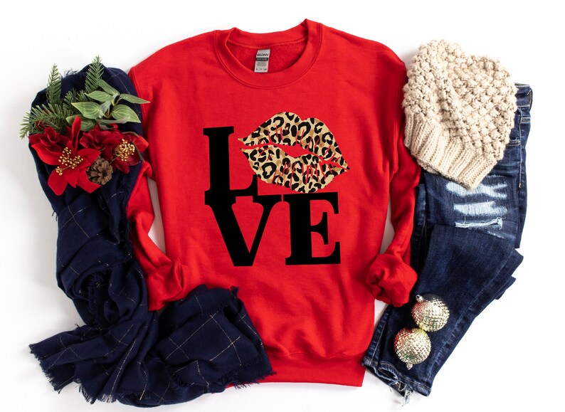 Pu&ograve; includere: Felpa rossa con una grafica nera "LOVE" e un design a labbra con stampa leopardata.