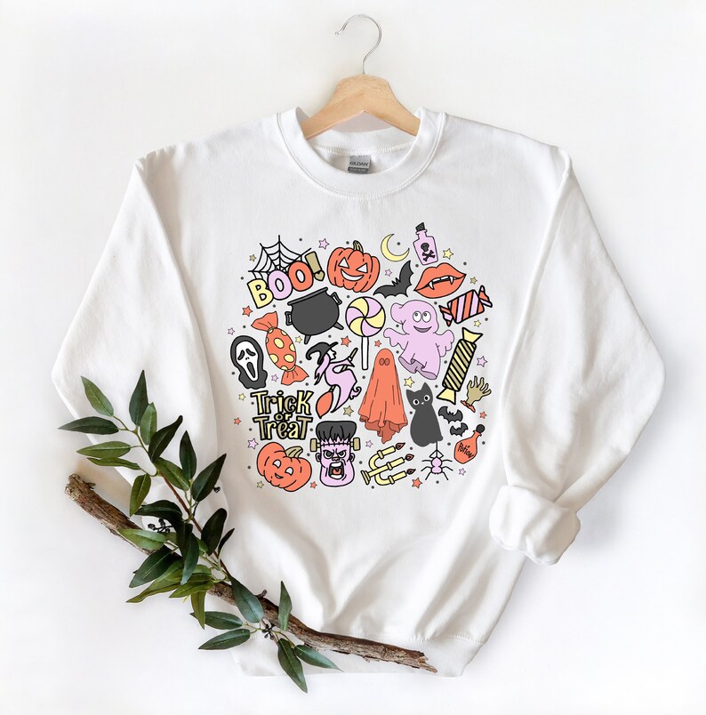 May include: White sweatshirt with a colorful Halloween-themed design featuring ghosts, pumpkins, bats, candy, and the words "Trick or Treat" and "Boo!"