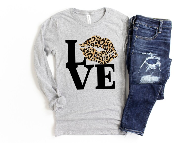 Pu&ograve; includere: Una maglietta grigia a maniche lunghe con una grafica nera "LOVE" e un design a labbra con stampa leopardata.