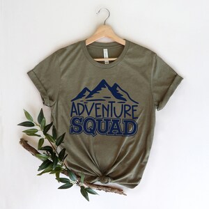 Puede incluir: Camiseta verde oliva con un gr&aacute;fico de monta&ntilde;a azul marino y el texto "Adventure Squad".