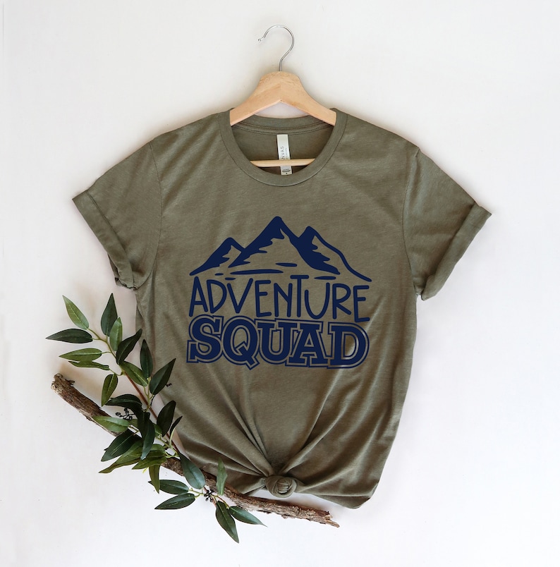 Puede incluir: Camiseta verde oliva con un gr&aacute;fico de monta&ntilde;a azul marino y el texto "Adventure Squad".