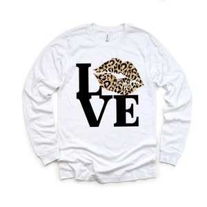 Pu&ograve; includere: Maglietta bianca a maniche lunghe con una grafica nera "LOVE" e un design a labbra con stampa leopardata.