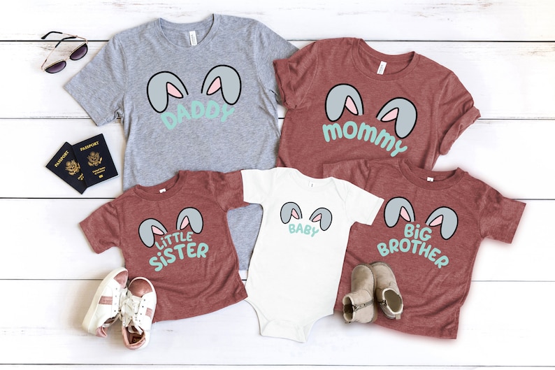 Pu&ograve; includere: Un set di cinque magliette con orecchie di coniglio e testo. Le magliette sono di vari colori, tra cui grigio, marrone e bianco. Il testo sulle magliette recita "Pap&agrave;", "Mamma", "Beb&egrave;", "Sorellina" e "Fratello maggiore".