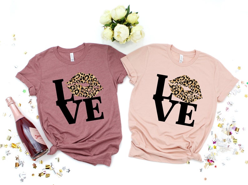 Pu&ograve; includere: Due magliette con la parola "LOVE" in lettere nere e un design a labbra con stampa leopardata. Le magliette sono color malva e rosa chiaro.