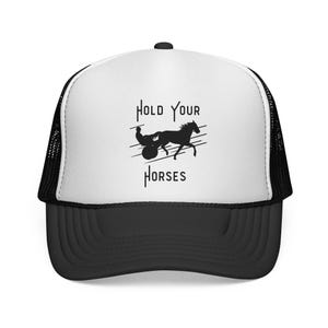 May include: A black and white trucker hat with a curved peak. The front panel is white and displays the text "Hold Your Horses" above a horse and driver silhouette. The back of the hat is black mesh.