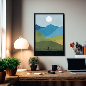 May include: A framed print of a minimalist landscape with a blue, green, and yellow color scheme. The print depicts a person running across a field with mountains in the background. The print is hanging on a white wall above a wooden desk with a laptop, a mug, and plants.