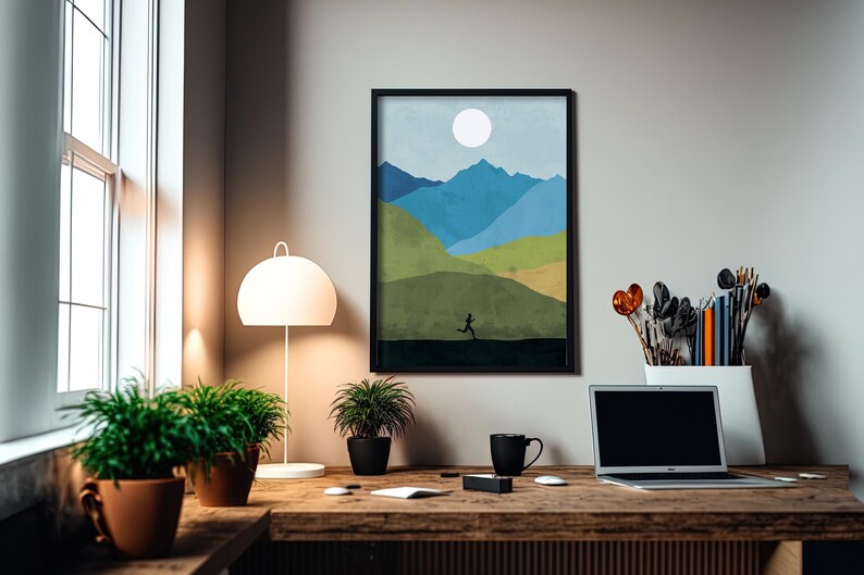 May include: A framed print of a minimalist landscape with a blue, green, and yellow color scheme. The print depicts a person running across a field with mountains in the background. The print is hanging on a white wall above a wooden desk with a laptop, a mug, and plants.