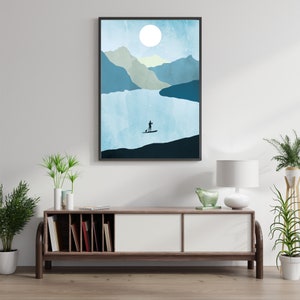 May include: Abstract art print featuring a serene mountain lake scene. A silhouetted figure paddles a stand-up paddleboard on the water under a large white moon. The artwork is framed in a black border and evokes a sense of tranquility.
