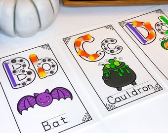 May include: Three Halloween-themed alphabet cards with letters B, C, and D. Each letter is outlined with googly eyes and candy corn. The cards also feature a bat, a cauldron, and a donut.