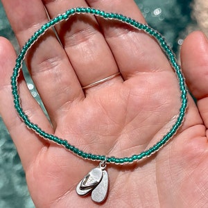 May include: A green beaded bracelet with a silver flip-flop charm.