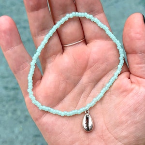 May include: A light blue beaded bracelet with a silver seashell charm.