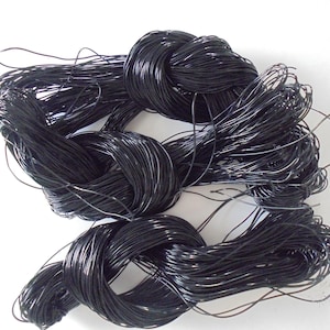 Pode incluir: Uma grande bobina de cordão encerado preto. O cordão está enrolado firmemente e parece ser feito de um material durável.