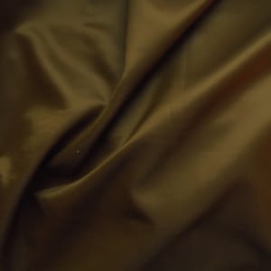 May include: A close-up of a smooth, dark brown fabric with a soft, silky texture. The fabric is folded and draped, creating a luxurious and elegant look.