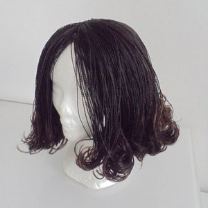 May include: A dark brown wig with small braids styled in loose curls. The wig is on a white mannequin head.