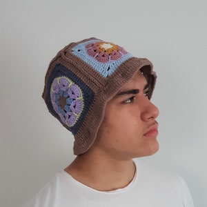 May include: A brown crocheted bucket hat with colorful granny squares. The hat has a light blue, purple, and pink flower design.