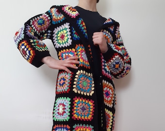 Könnte beinhalten: Ein langer schwarzer Häkelcardigan mit einem bunten Granny-Square-Muster. Der Cardigan hat eine Kapuze und ist vorne offen.