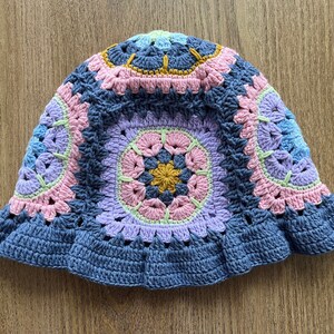 May include: A crocheted hat with a blue brim and a colorful floral pattern in shades of pink, purple, green, and yellow.