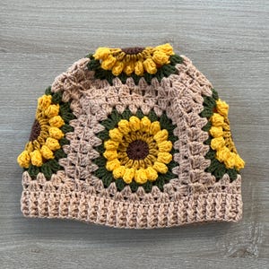 May include: A crocheted hat with a brown, green, and yellow sunflower design.