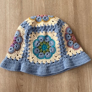May include: A crocheted hat with a blue brim and a cream colored top. The top features a circular pattern with colorful accents.