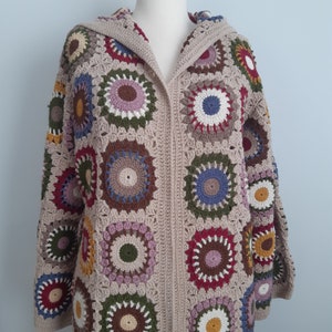 May include: A beige crocheted cardigan with a hood, featuring a colorful geometric pattern of circles in shades of red, blue, green, brown, and white.