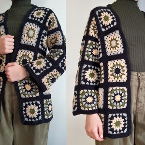 Könnte beinhalten: Eine schwarze Häkeljacke mit einem Granny-Square-Muster in Grün-, Beige- und Weißtönen. Die Jacke hat einen V-Ausschnitt und lange Ärmel.