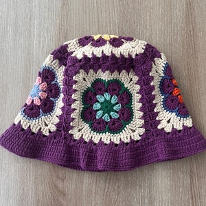 May include: A purple crochet bucket hat with a white and cream crocheted design featuring colorful flowers.