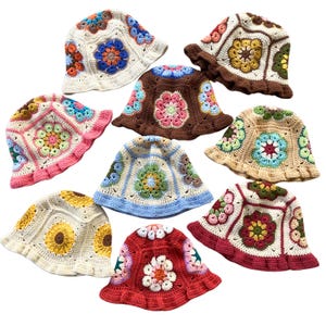 Może przedstawiać: Dziewięć dzianych czapek typu bucket w różnych kolorach i wzorach. Czapki mają różne wzory kwiatowe w odcieniach różowego, niebieskiego, żółtego, czerwonego i brązowego.